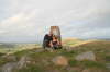 Derek & Suzanne sheltering behind Trig Point
